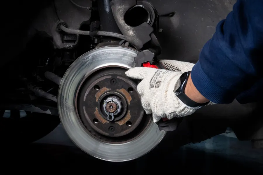 A gloved hand on a car's brake rotor and caliper