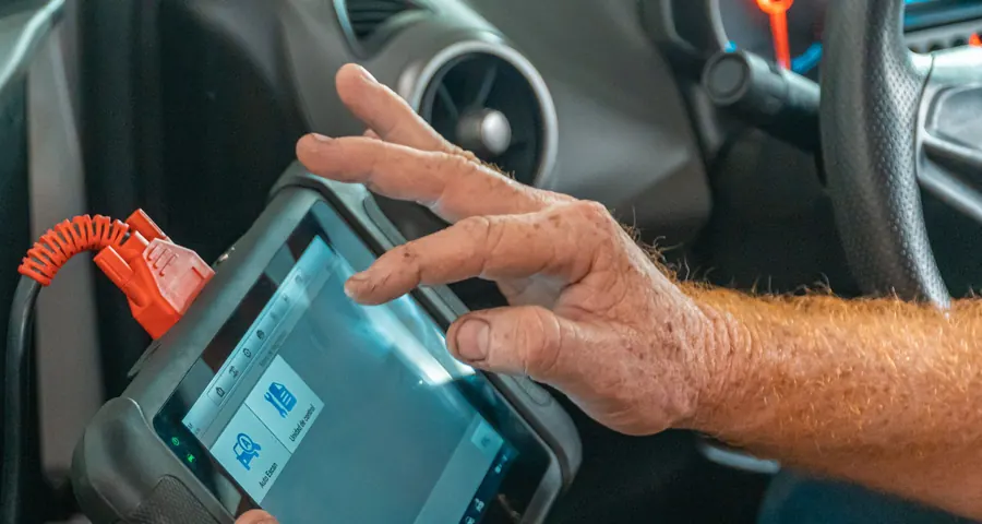 A technician using a diagnostic scan tablet plugged into a car