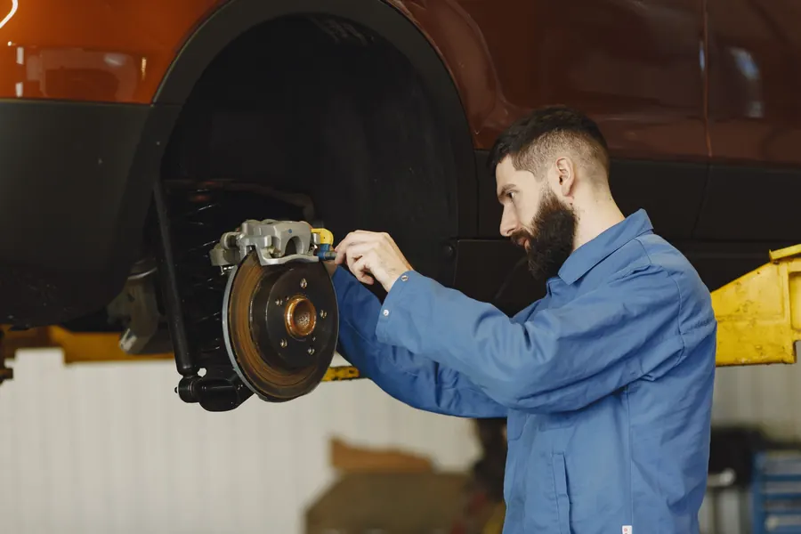 A technician in a blue work shirt measuring a front brake rotor on a car raised on a lift