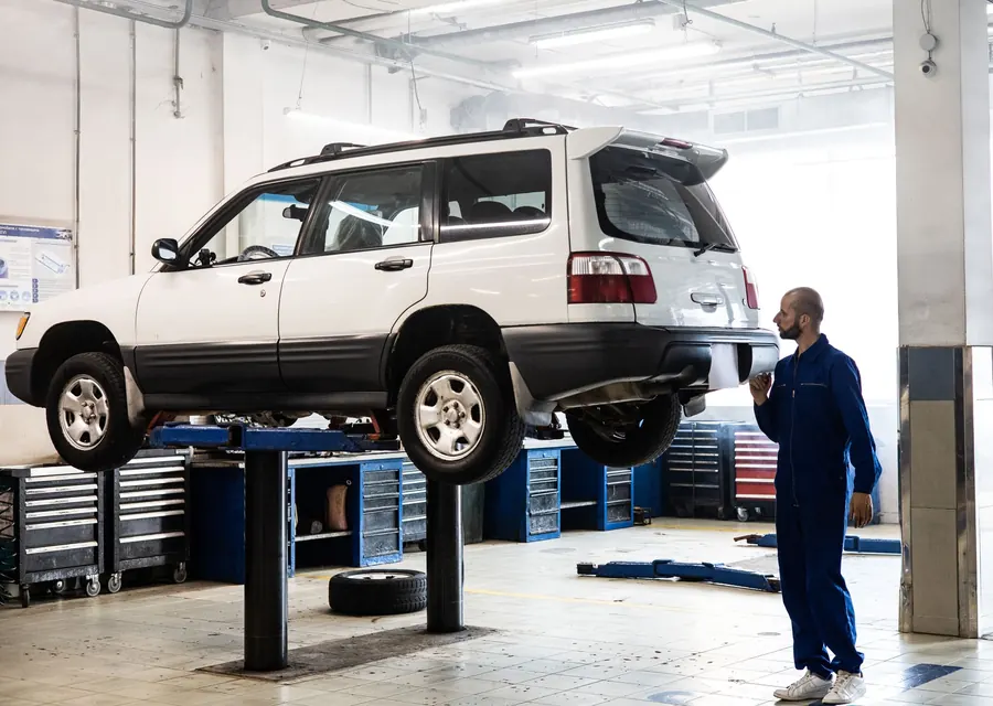A technician inspecting a white SUV raised on a lift