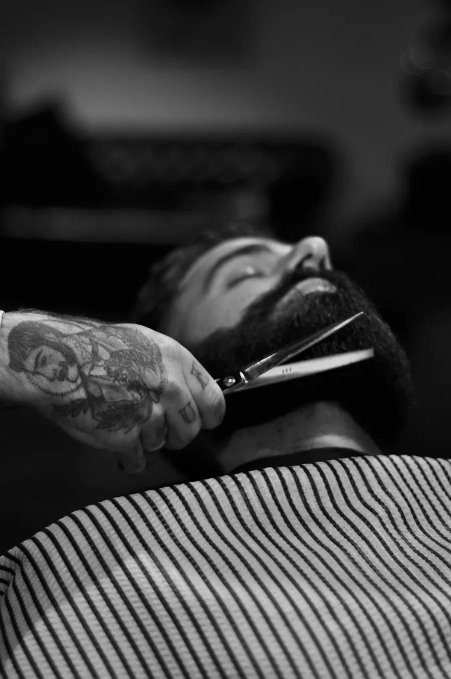 Black and white photo of a barber shaping a full beard with scissors