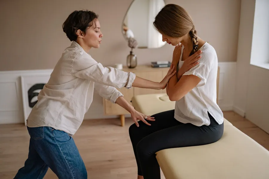 A clinician guides a seated patient through a mobility test beside a treatment table