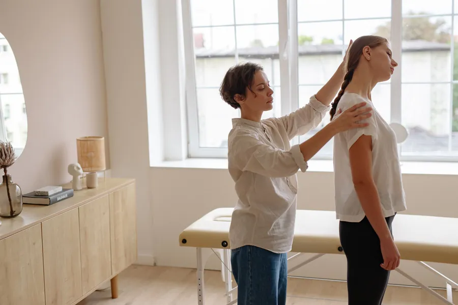 A chiropractor checks a patient's shoulder and posture in a bright, quiet treatment room