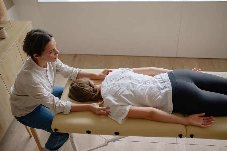 A massage therapist works on a patient's back as she lies face down on a cushioned table