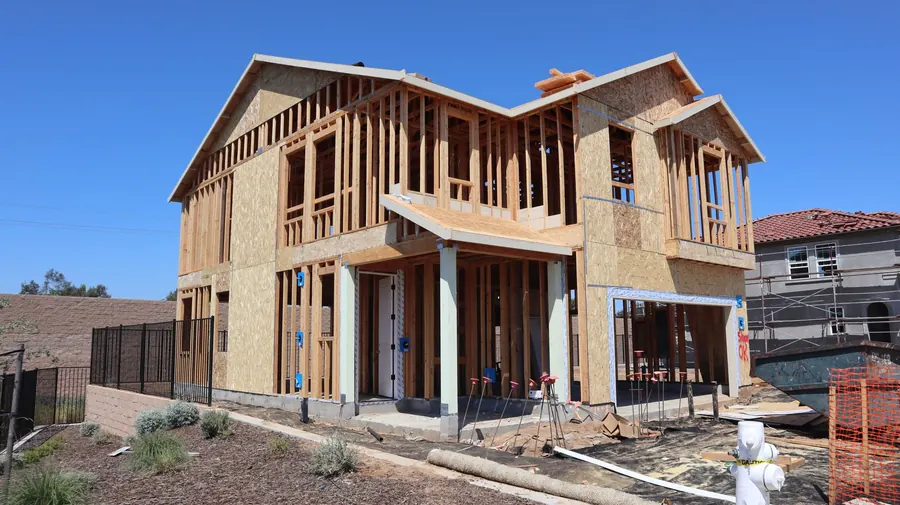 A two-story wood-framed house under construction against a clear sky