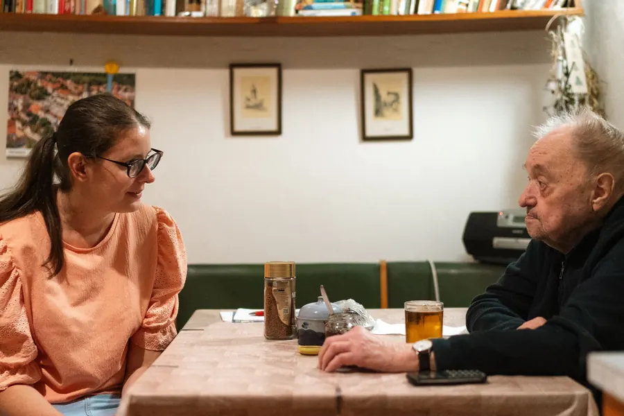 A young woman and an older man talking over tea at a kitchen table