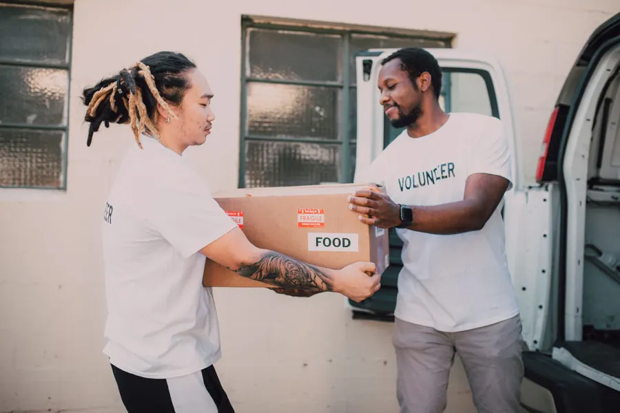 Two volunteers passing a food box out of a white delivery van