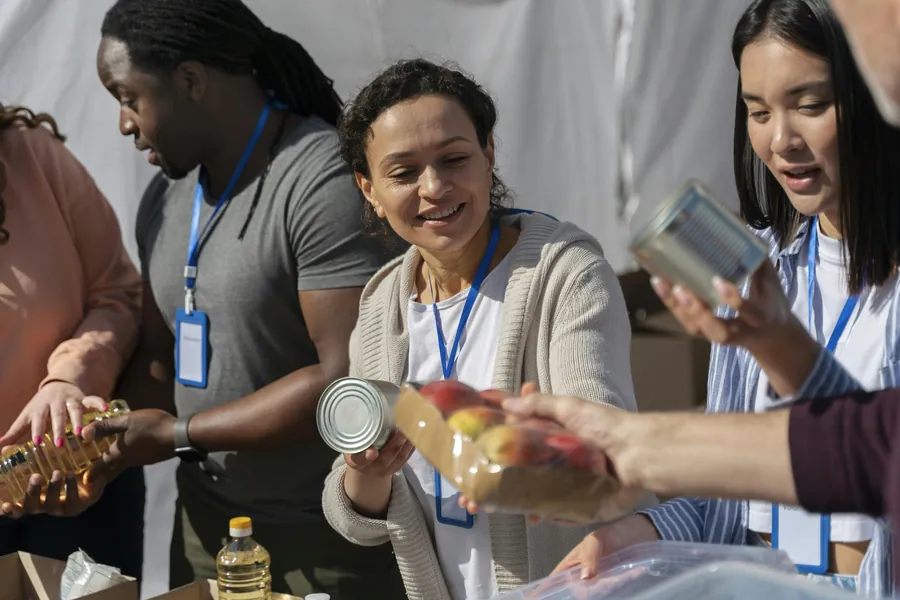 Smiling volunteers with name badges passing canned goods and fresh fruit down a distribution table