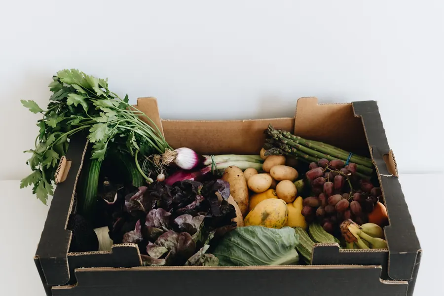 A cardboard box packed with leafy greens, potatoes, beets and fresh fruit