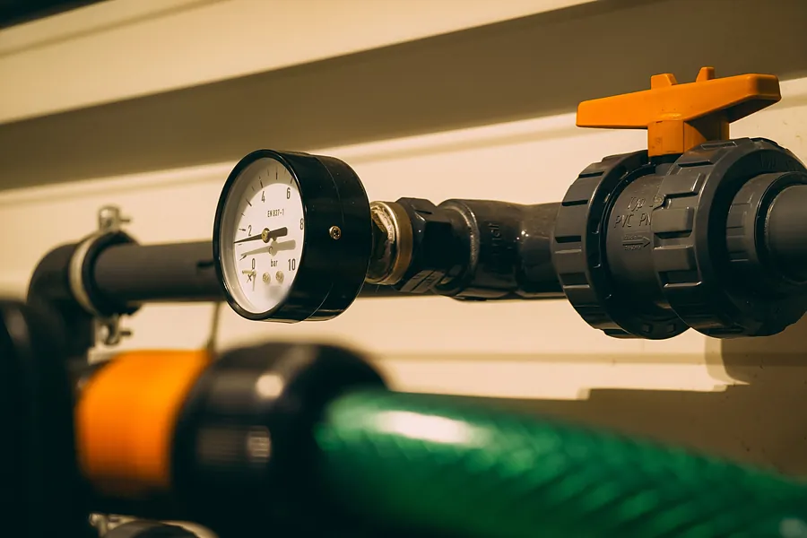 Close-up of a pressure gauge, PVC union and orange-handled valve on equipment-pad plumbing