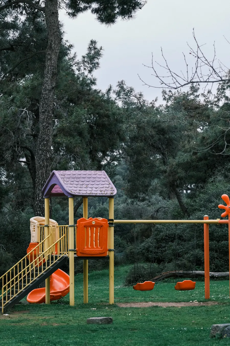 A wooden play structure with a slide and climbing ladder among shade trees
