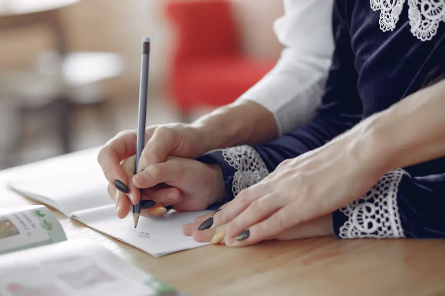 An adult's hand gently guiding a child's hand writing in a notebook
